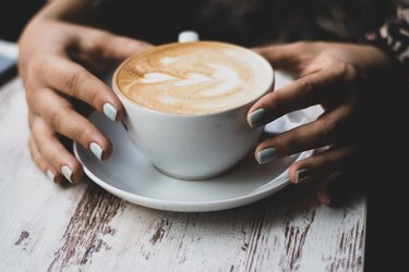 person holding a late in a cup on wooden table