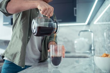 Close up of a person pouring coffee into a glass in their kitchen