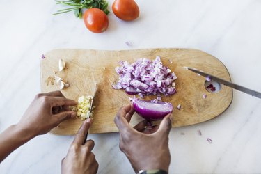 Cropped image of couple of hands cutting onion and garlic on cutting board in kitchen