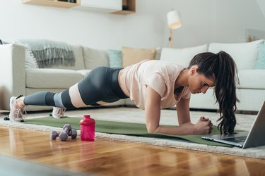 woman holding a plank and doing an ab workout in her living room with her laptop