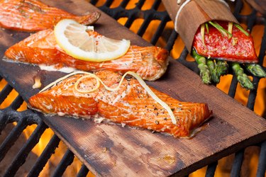 Three grilled tyrosine-rich salmon fillets on a cedar plank over a fire on the grill.