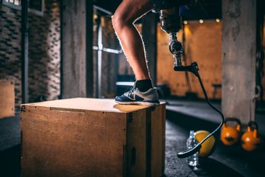 close up of a man with a prosthetic leg doing the step-up exercise on a wooden box in the gym