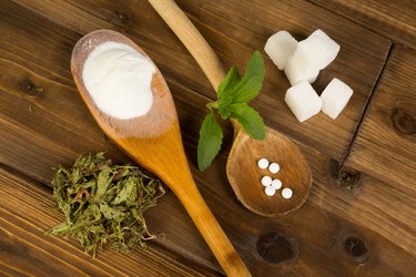 Sugar and stevia in wooden spoons on wooden table