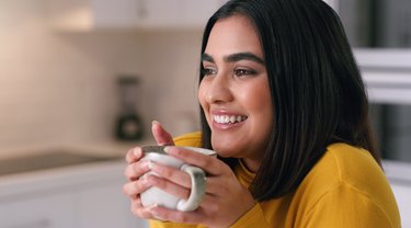 Young person in a yellow sweater with a big smile on their face while holding a mug of coffee or tea