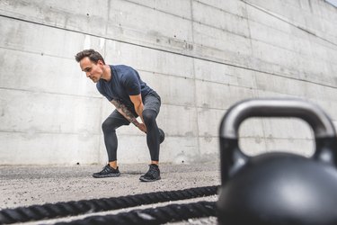 caucasian man doing kettlebell swing outside in front of a concrete wall