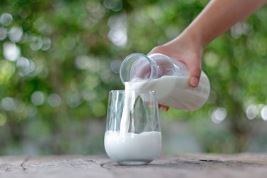 Woman pouring a glass of full-fat milk.