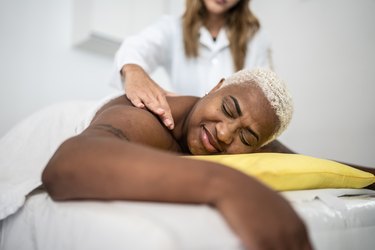 a person lying on a massage table supported by a yellow pillow gets a back massage
