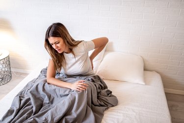 女人在床上抱着背部酸痛的背阔肌疼痛晚上从睡姿睡觉后