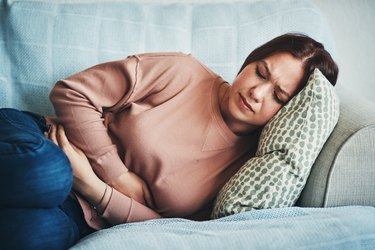 a woman lying on the couch holding her side because she has upper left abdominal pain