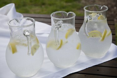 Three pitchers of ice water with lemon slices on white napkin