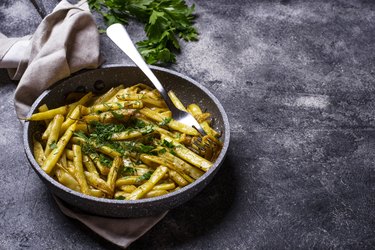 Stewed yellow wax beans in a pan over dark gray background.