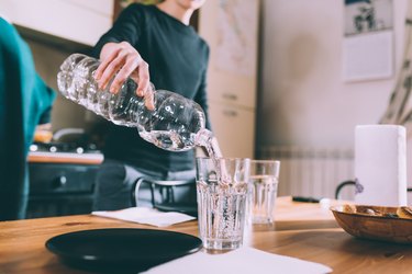 Cropped shot of young woman pouring water at kitchen table
