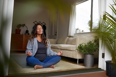 Mature woman meditating in her living room, as a natural remedy for hot flashes