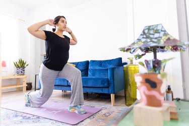 Person wearing a black T-shirt and gray sweatpants performing a lunge in their living room as part of a postpartum strength workout.