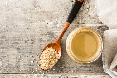 Tahini and sesame seeds on wooden table