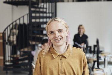 Portrait of smiling non-binary computer programmer with dyed long hair at tech startup office