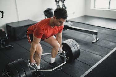 caucasian man in red shirt doing a trap bar deadlift in a gym