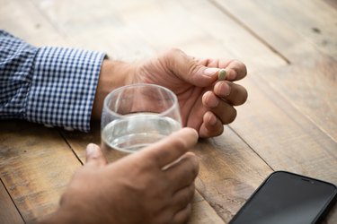 Close up of person's hands holding a pill and glass of water while wondering about the Adipex BMI calculator