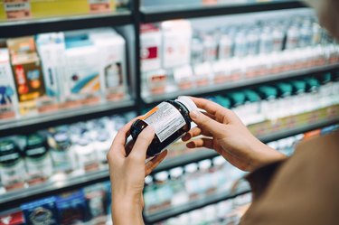 close view of a person's hands holding a bottle of biotin, checking the dosage instructions