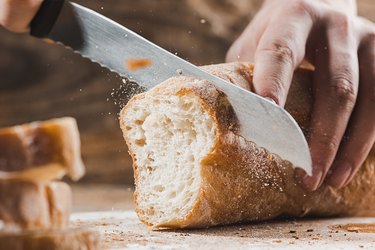 Whole grain bread put on kitchen wood plate with a chef holding gold knife for cut