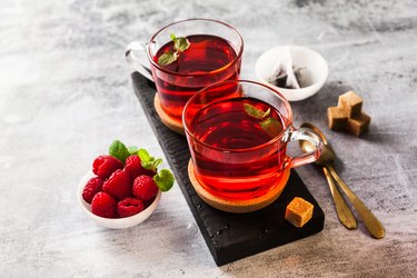 Hot red raspberry tea in two transparent cups on a stone table. Fresh berries, cubes of cane sugar and a bag of tea