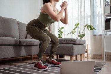 Woman performing squat exercise doing lower-body workout video at home