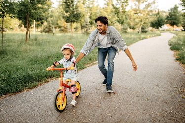 a father helping his daughter learn how to ride a bike outdoors