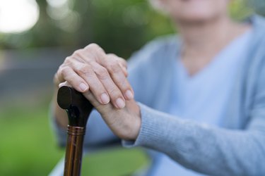 Close-up of senior woman's hands holding her walking sticks sitting at park.