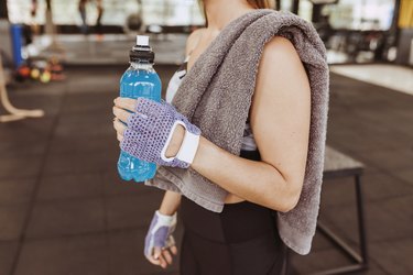 Young unrecognizable fit person in gym drinking isotonic drink