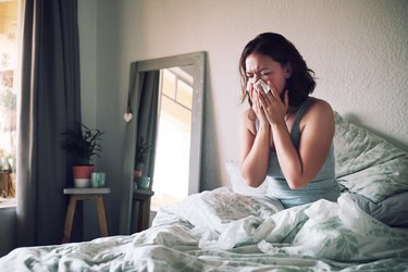 woman with morning allergies blowing her nose in bed