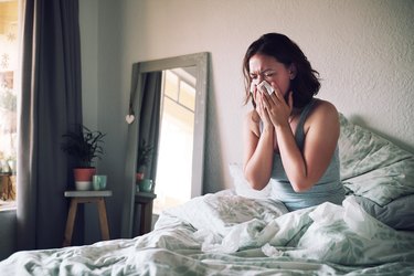 早上过敏的女人在床上擤鼻涕