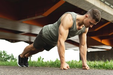Muscular man is doing knuckle push-ups during calisthenic workout on a street