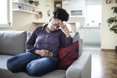 a person sitting on the couch with stomach pain holding their stomach and head