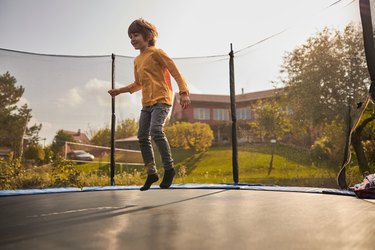 Child jumping on a trampoline outside in the backyard.