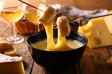 cheese fondue with baguette and wine on wood table