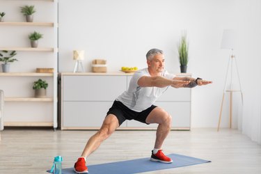 Older adult wearing a white T-shirt and black shorts doing a side lunge as part of a low-impact Tabata workout.