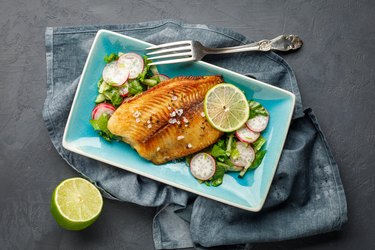 Grilled fish sea bass with fresh herbs, radish and lime in a rectangular blue plate.