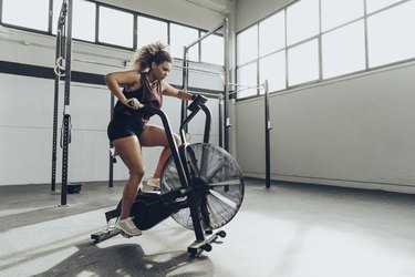 Young person with hair in a ponytail doing interval training on an air bike in an industrial-style gym