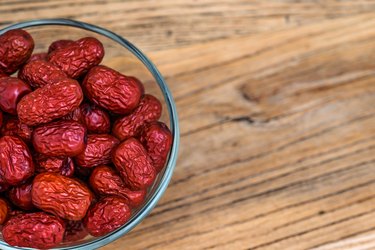 An overhead photo of a bowl of dry red jujubes on a wooden table