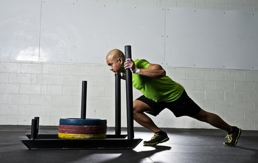 Athletic man pushing a prowler sled in the gym