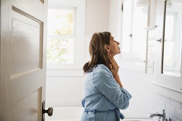 Person wearing a blue shirt looking at and touching their thyroid gland in the mirror