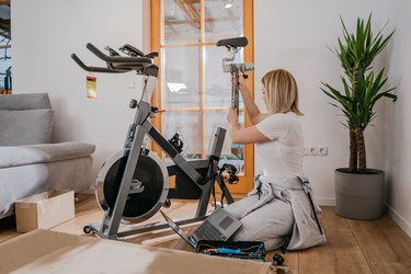 Woman assembling stationary bicycle in living room for at home cardio machine workout