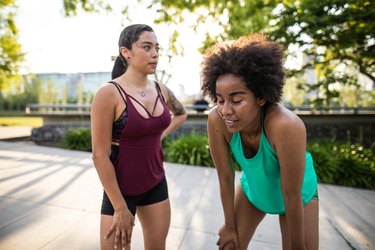 Two people in workout clothes resting in a park after a sweaty workout in hot weather