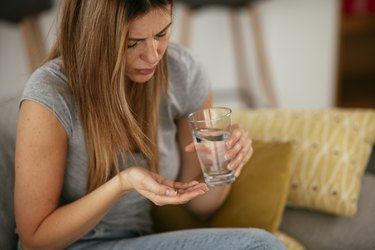 年轻女人生病在床上拿着一杯水。