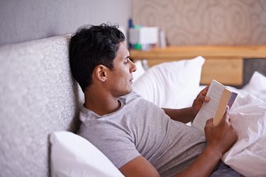 Man reading a book in bed to calm racing thoughts at night