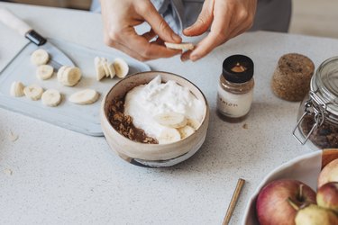 Hands Slicing a Banana into a bowl of high-protein skyr yogurt