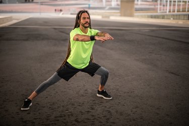 Person with long dreadlocks and a beard does a lateral lunge to stretch their inner thigh
