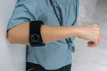 Person wearing black elbow brace with adjustable button to reduce pain on white background