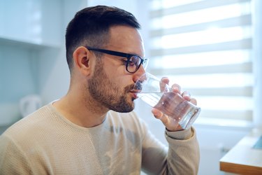 美丽的白人男子坐在餐桌边喝水的侧视图。