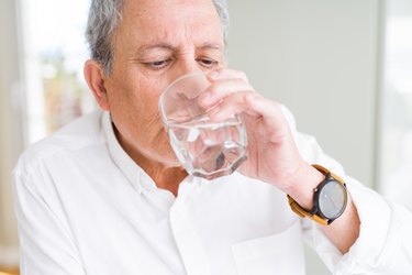 senior man drinking a fresh glass of water with magnesium citrate at home